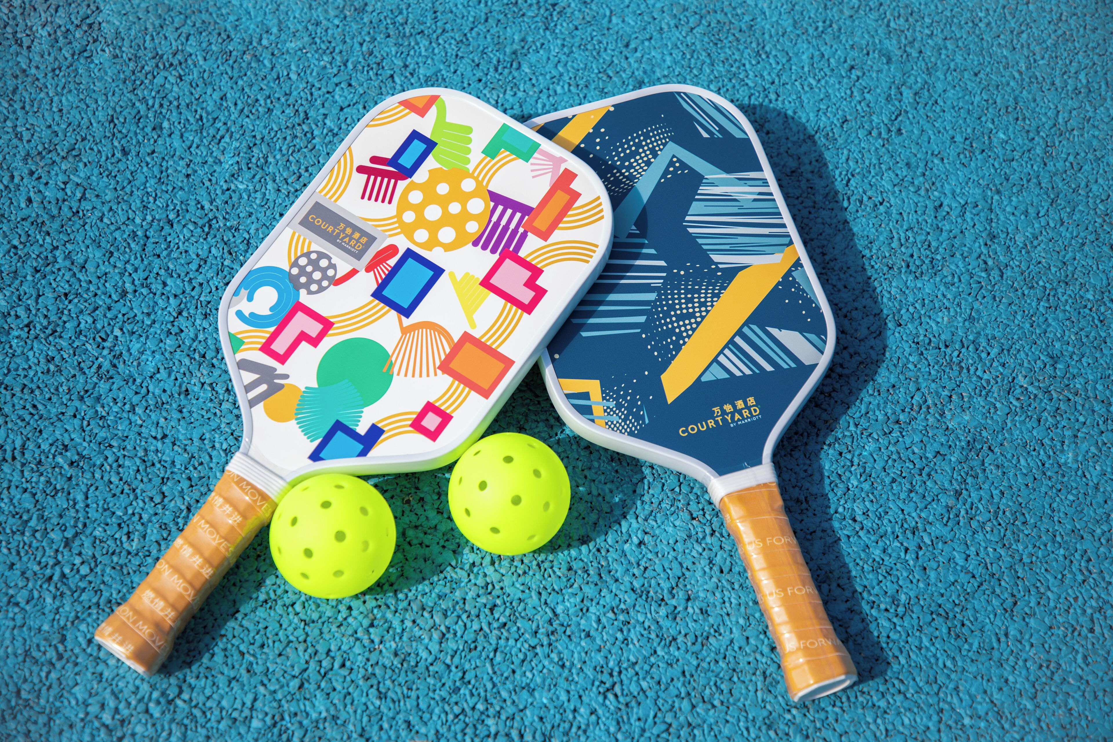 Two colorful badminton rackets and two bright yellow shuttlecocks on a blue textured surface.