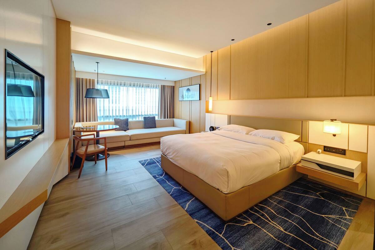 Een moderne hotelkamer met een groot bed, een zithoek met een tafel, en een groot raam met gordijnen.
