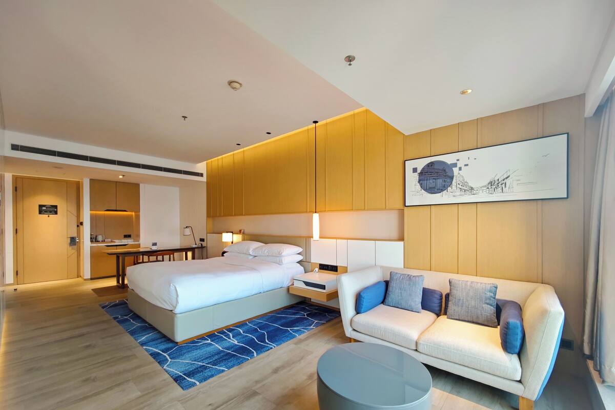 Een moderne hotelkamer met een bed, een bank, een kleine tafel en een bureau met stoel.