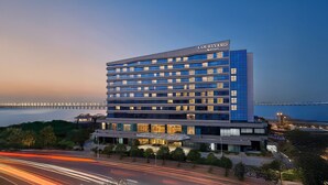 Een Courtyard Marriott hotel met een modern design, meerdere verdiepingen en een uitzicht op het water en een brug in de achtergrond.