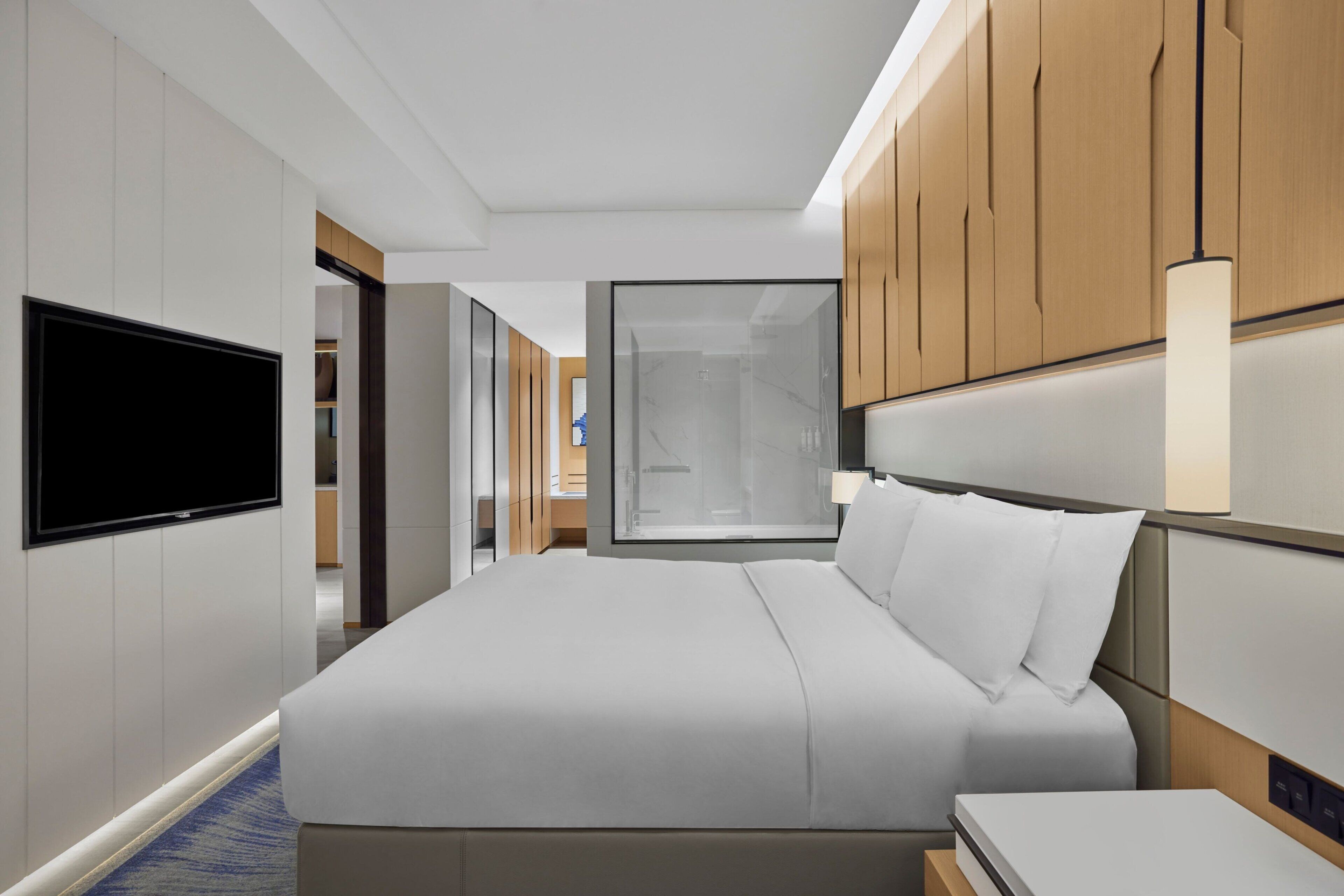 Ein modernes Hotelzimmer mit einem großen Bett, einem flachbildfernseher an der Wand und einem großen Fenster mit Blick ins Innere.