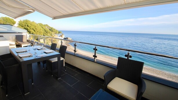 An outdoor dining area with a view of the sea, a table set with glasses, and wicker chairs. - Athena beauty in Altea (Altea)