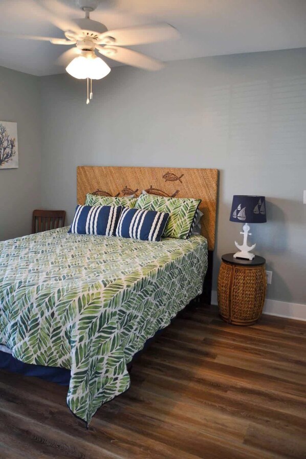 A bedroom with a bed, a ceiling fan, a nightstand, and a wall-mounted lamp.