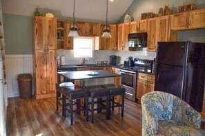 A kitchen with wooden cabinets, a central island with stools, a refrigerator, and a microwave.