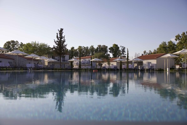 Zona de piscina con sillas de descanso y sombrillas, rodeada de edificios con techos de tejas rojas y paredes blancas.