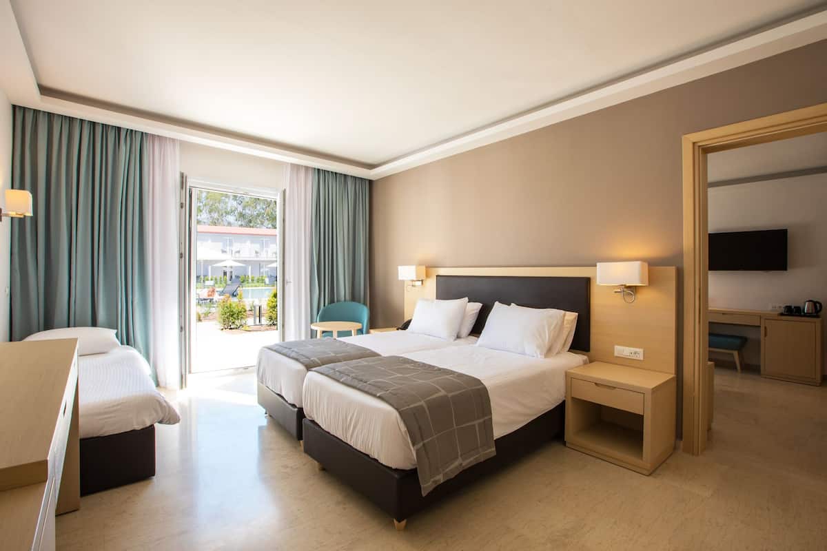 A hotel room with a bed, bedside tables, a chair, a TV, and a view of the outside.