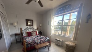 Une chambre avec un lit, une fenêtre, un ventilateur de plafond et une pancarte indiquant « Maison de plage ».