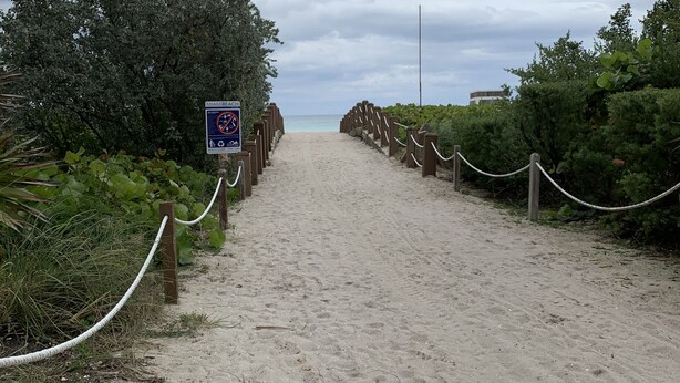 Un sentier de plage sablonneux avec un panneau indiquant qu'il est interdit de se baigner dans cette zone.