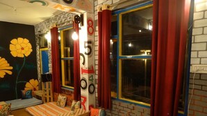 A cozy room with a brick wall, large windows with red curtains, and a colorful mural. - EL PROFESOR MCLEODGANJ (Dharamshala)