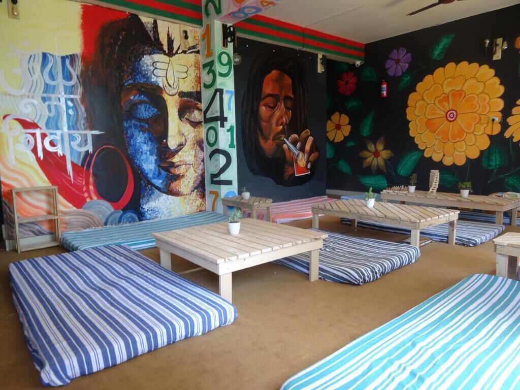 Una habitación con cojines a rayas azules y blancas, mesas de madera y un mural con diseños florales y abstractos.