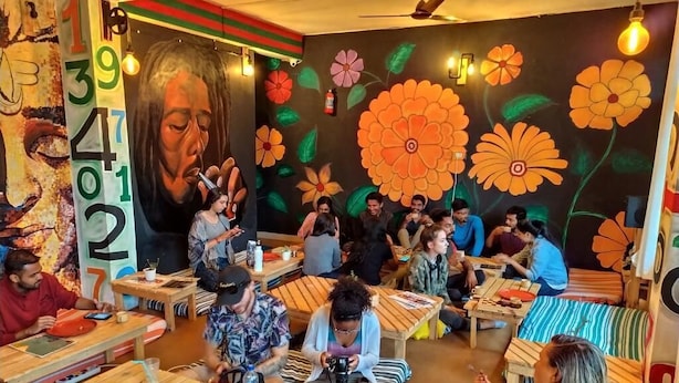 A dining area with wooden tables and benches, surrounded by walls with large floral murals and a prominent number mural. - EL PROFESOR MCLEODGANJ (Dharamshala)