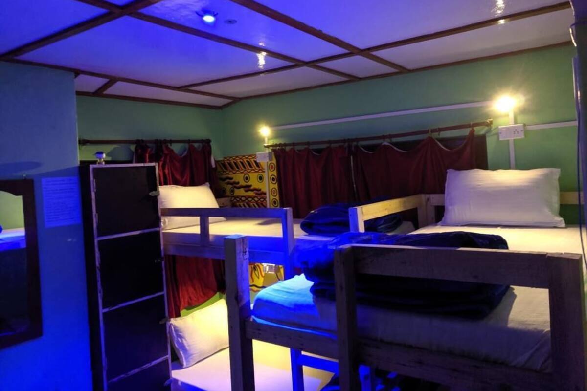 A dormitory room with bunk beds, a shelf, and curtains.
