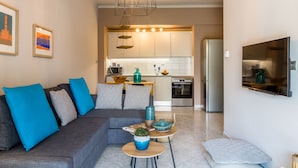 A modern living room with a grey sofa, blue cushions, a small round table with a plant, and a TV on the wall. - Nautilus Charm Apartment (Chania)