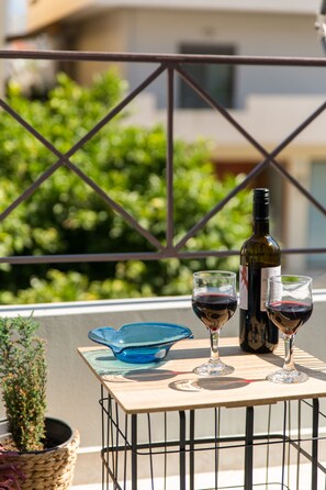 A balcony with a table holding a wine bottle and two glasses of red wine, a blue glass bowl, and a potted plant. - Nautilus Charm Apartment (Chania)