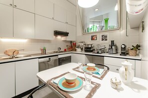 A modern kitchen with white cabinets, a dishwasher, a coffee maker, and a dining table set with plates and glasses.