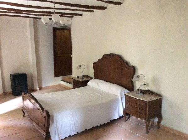 A bedroom with a wooden bed, two bedside tables, a nightstand, and a wall-mounted light fixture.