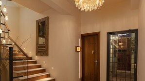 Un hall d’entrée spacieux avec un escalier en bois, un grand lustre et une porte en verre.