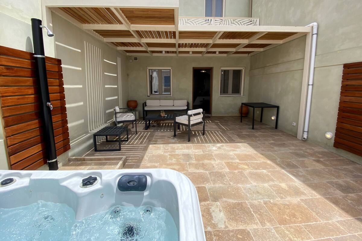 A patio area with a hot tub, outdoor seating, and a covered wooden deck.