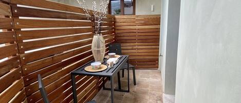 An outdoor patio with a wooden slatted wall, a table with chairs, and a vase with branches.
