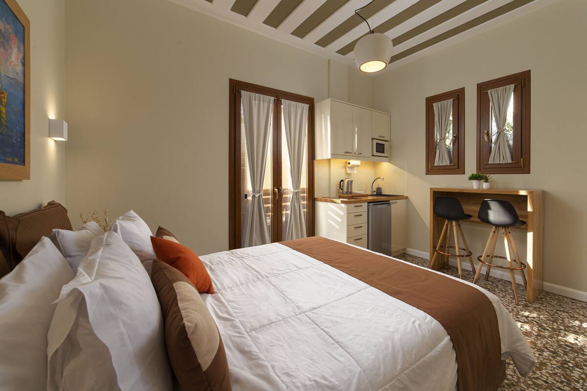 A bedroom with a bed, a desk, and a kitchenette.