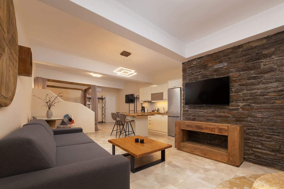 A modern living room with a sofa, a coffee table, and a stone wall with a TV.