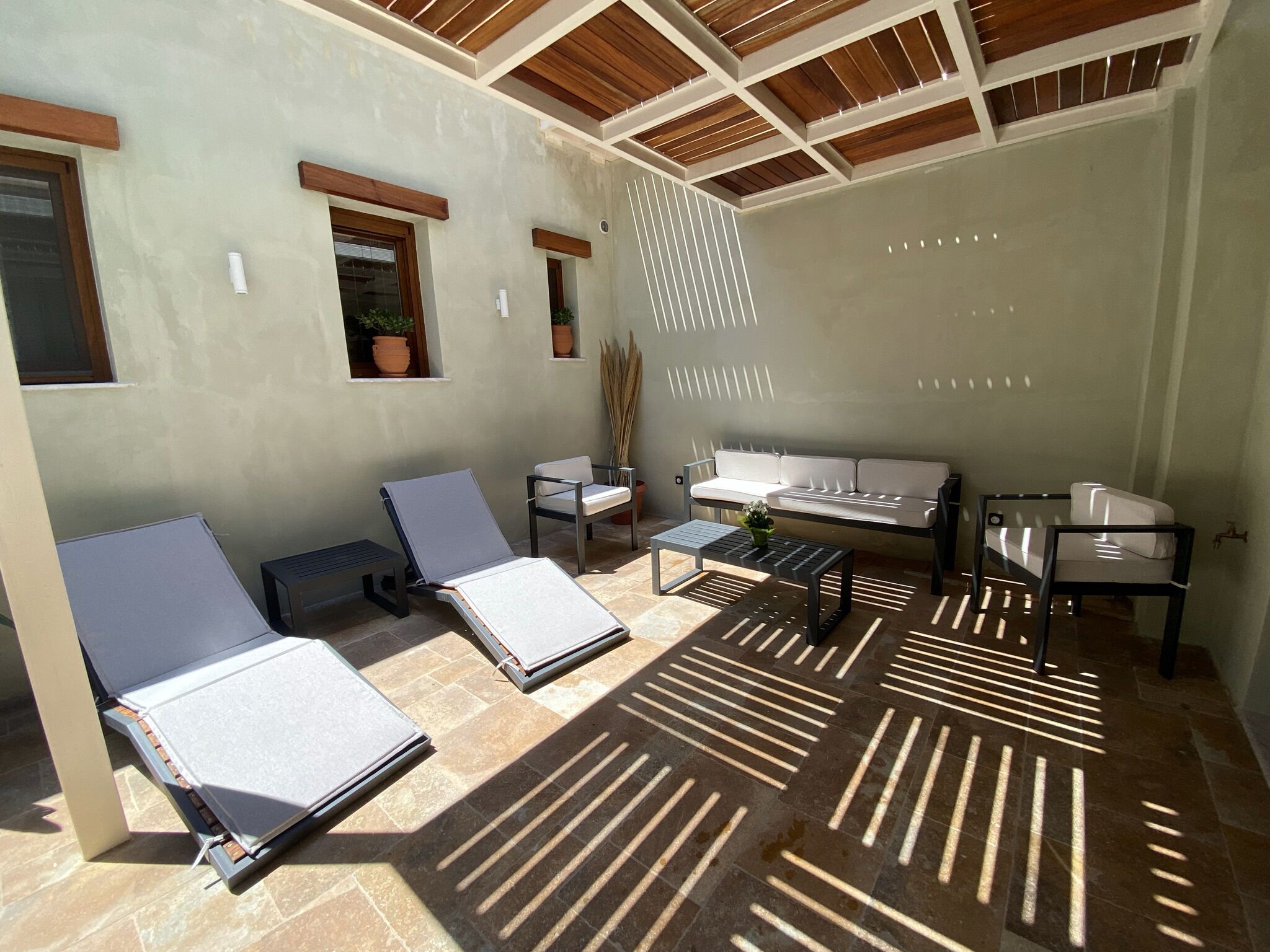 A sunlit patio with two lounge chairs, a sofa, and a small table.