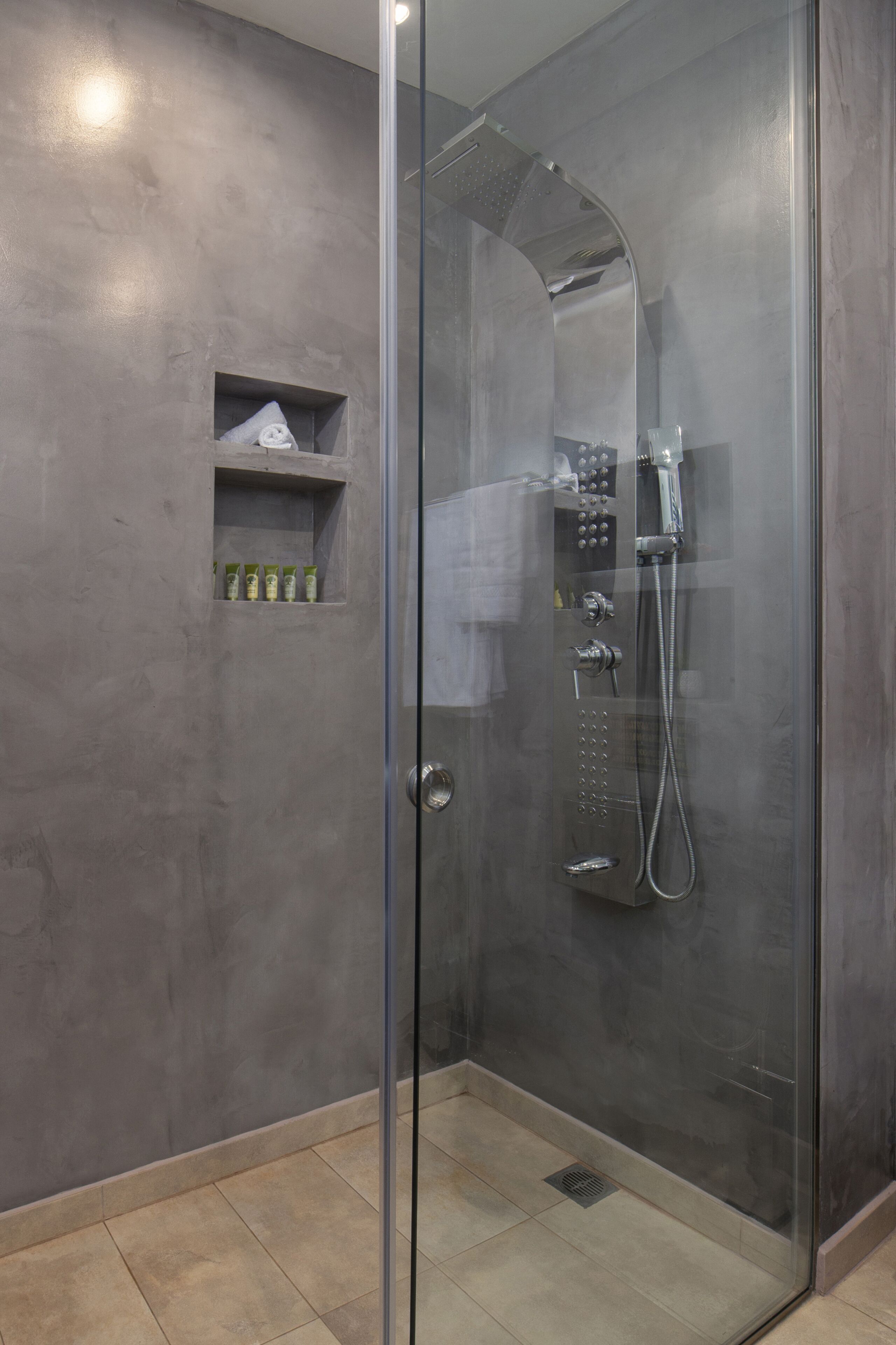 A glass-enclosed shower with a handheld showerhead and a wall-mounted control panel.