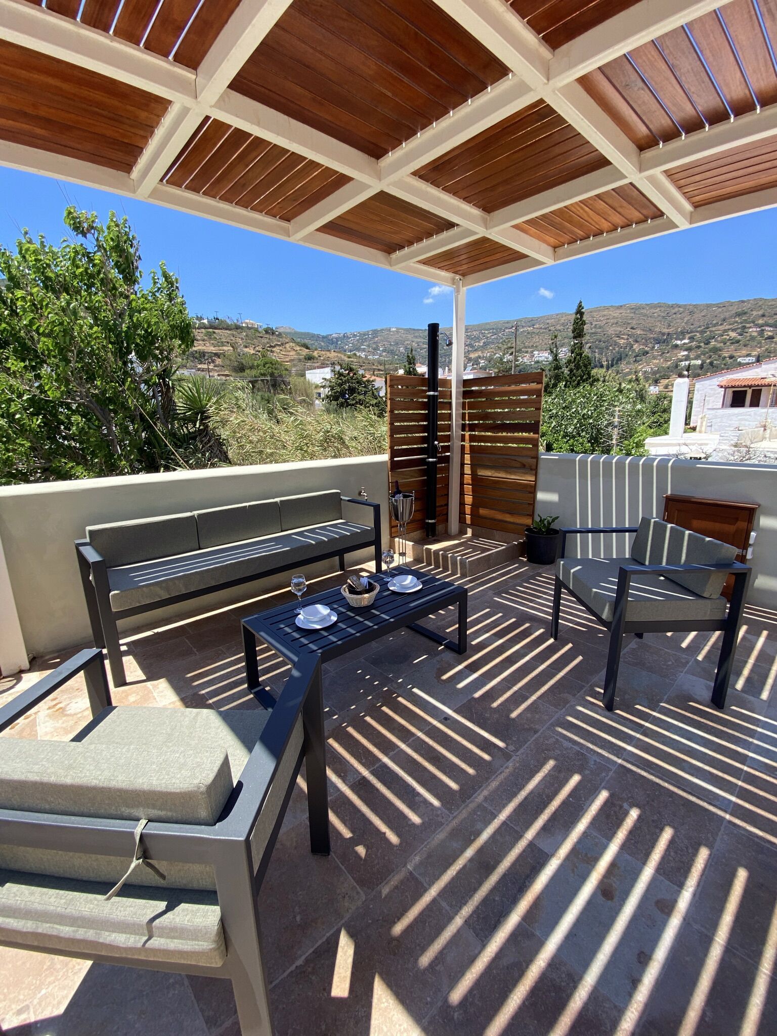Un espace extérieur aménagé en terrasse, avec une pergola en bois, une table dressée avec des assiettes et des verres, et un banc.