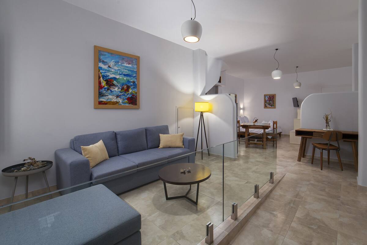 A modern living room with a blue sofa, a glass coffee table, and a dining area with a wooden table and chairs.