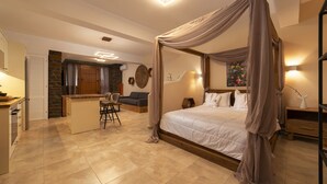 Une chambre à coucher avec un lit à baldaquin, un coin salon avec un fauteuil et une table, et un coin cuisine avec un comptoir et des tabourets.
