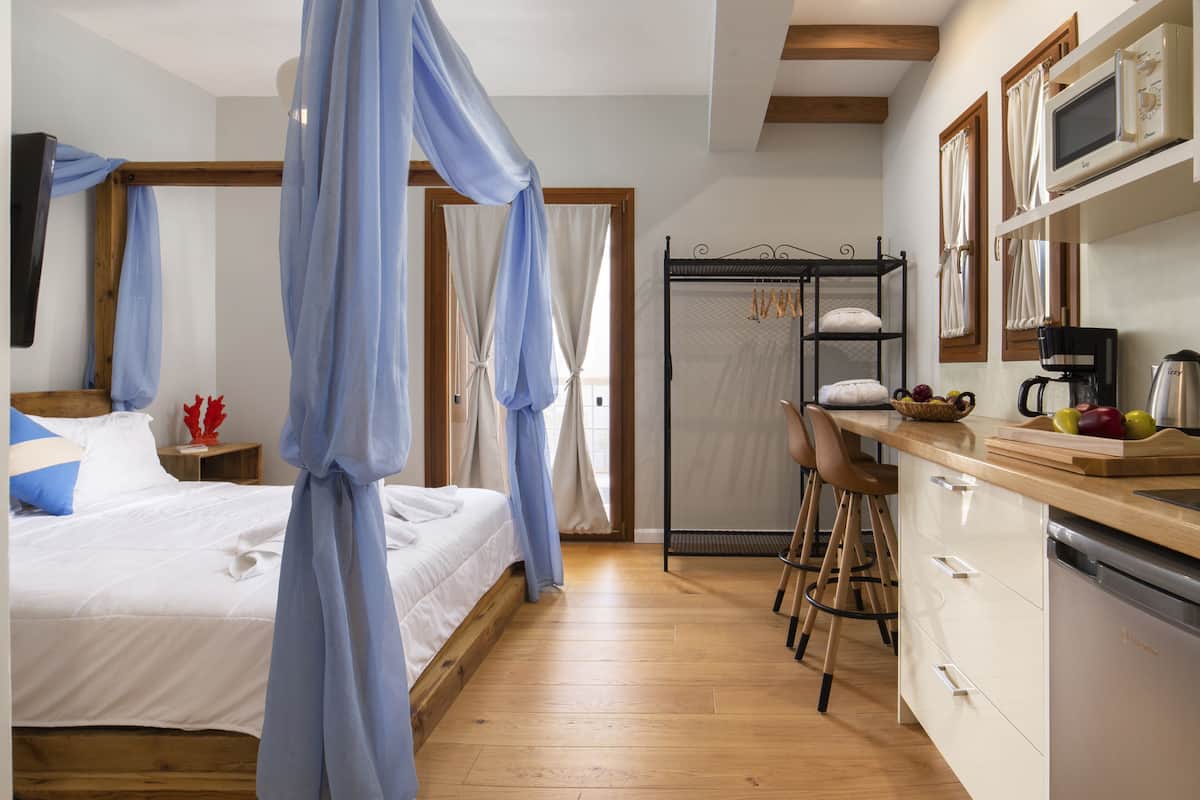 A bedroom with a bed, a bedside table, a nightstand, a window with curtains, and a wooden ceiling.