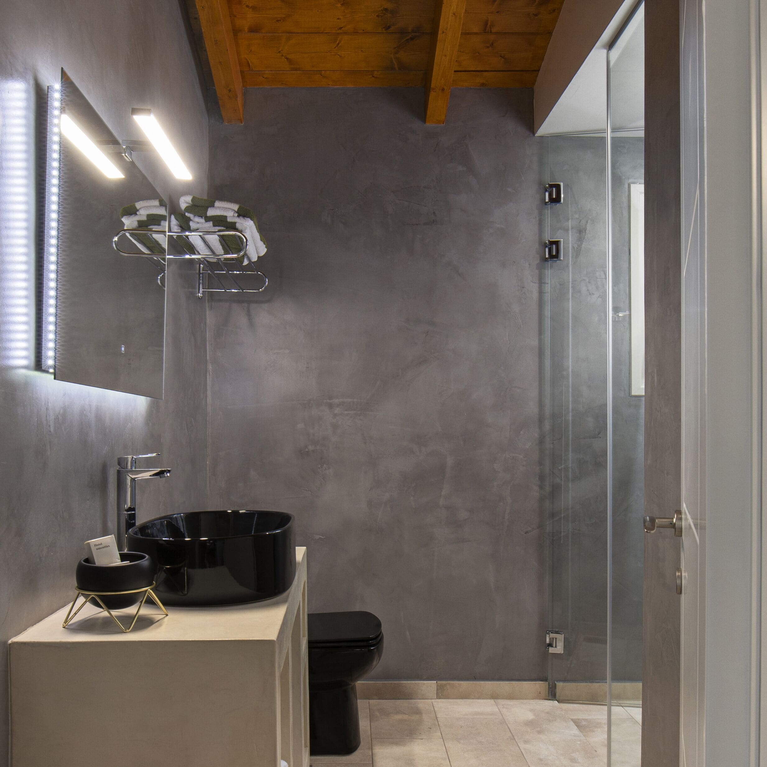 A modern bathroom with a large mirror, a black sink, and a glass shower enclosure.