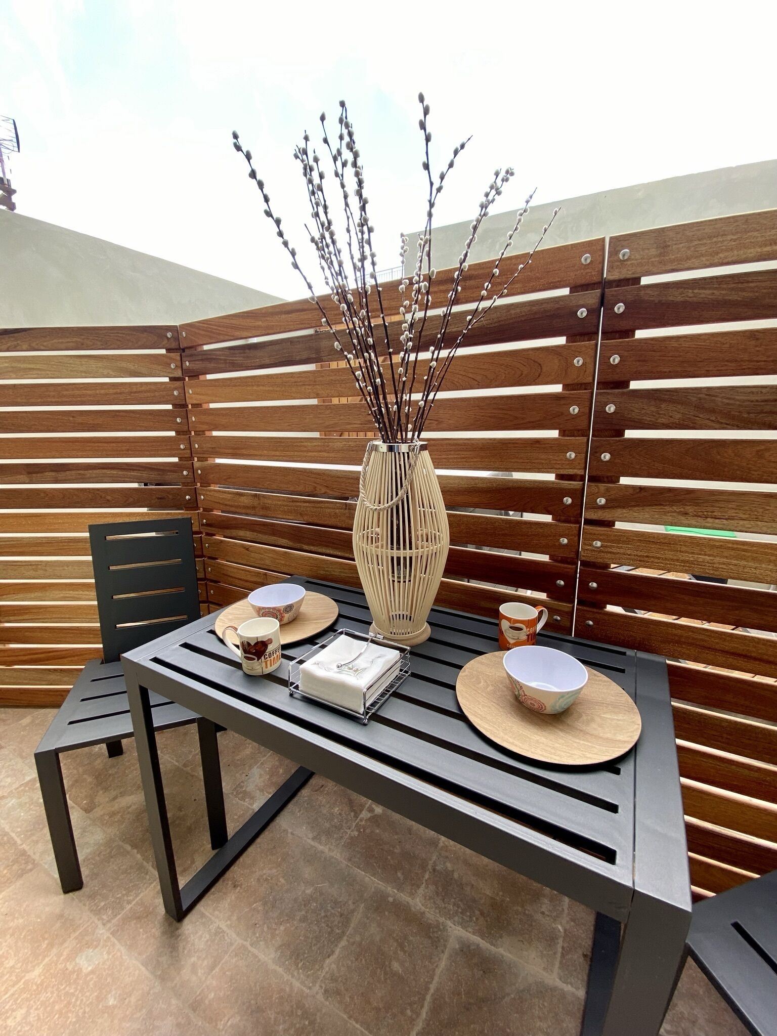 A modern outdoor dining area with a wooden slatted wall, a metal table, and chairs.