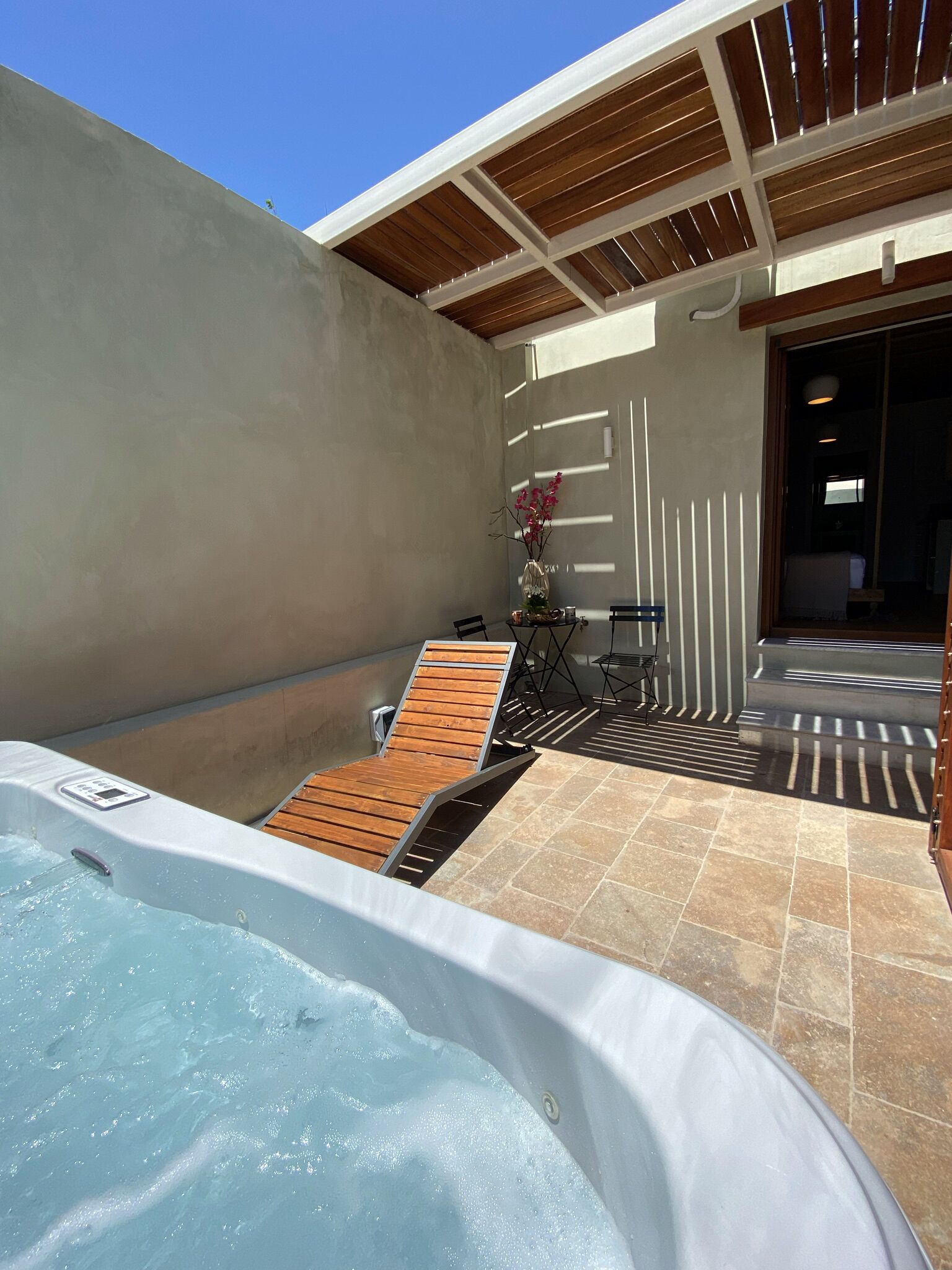 A hot tub with wooden loungers, a small table with a vase, and a pergola structure.