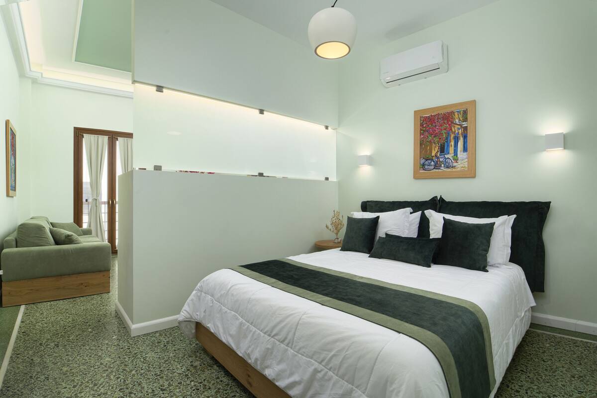 A bedroom with a bed, a bedside table, a lamp, a painting, and a window.