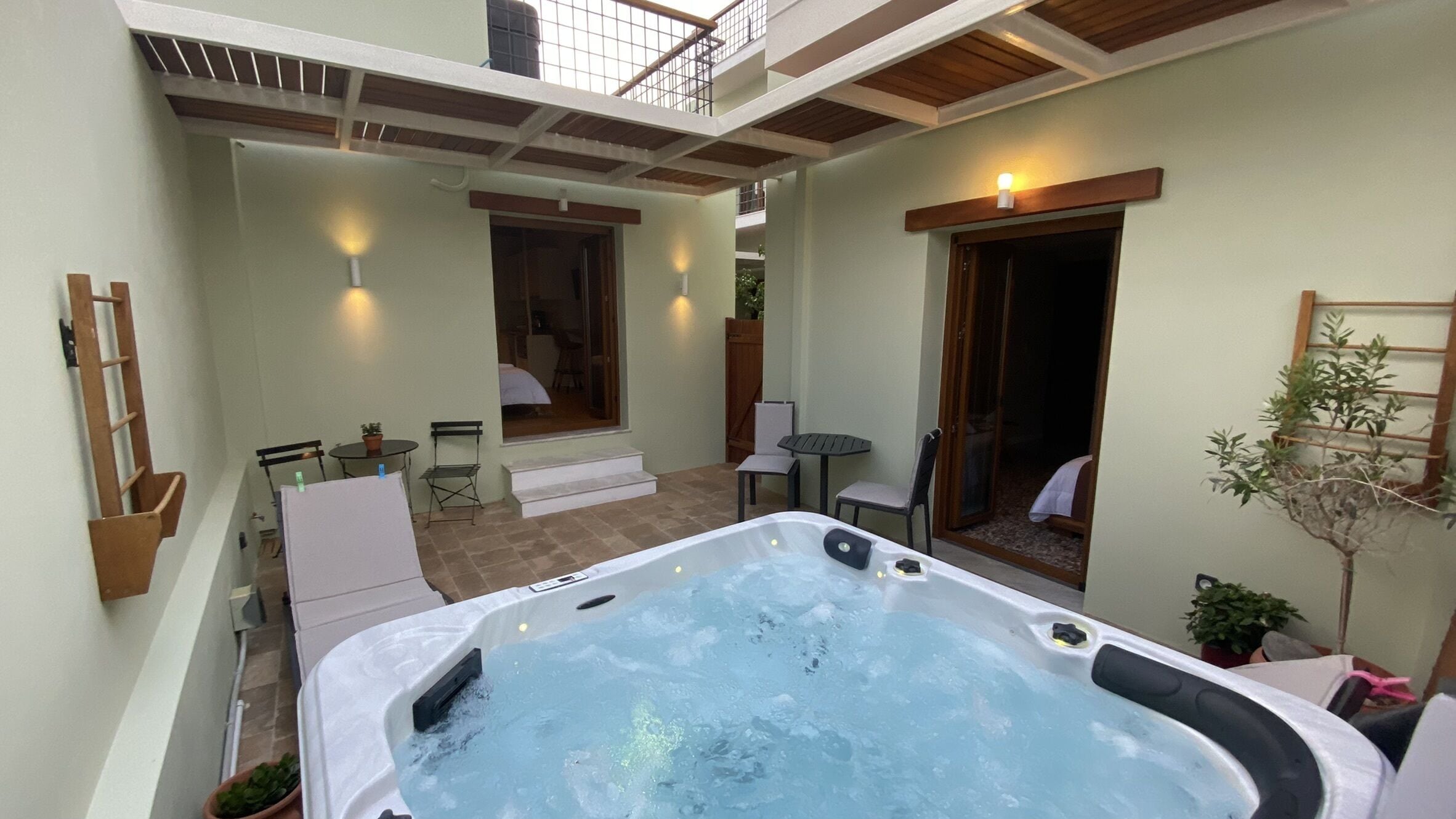 Un jacuzzi en un área exterior techada, con patio, asientos y vista al interior.