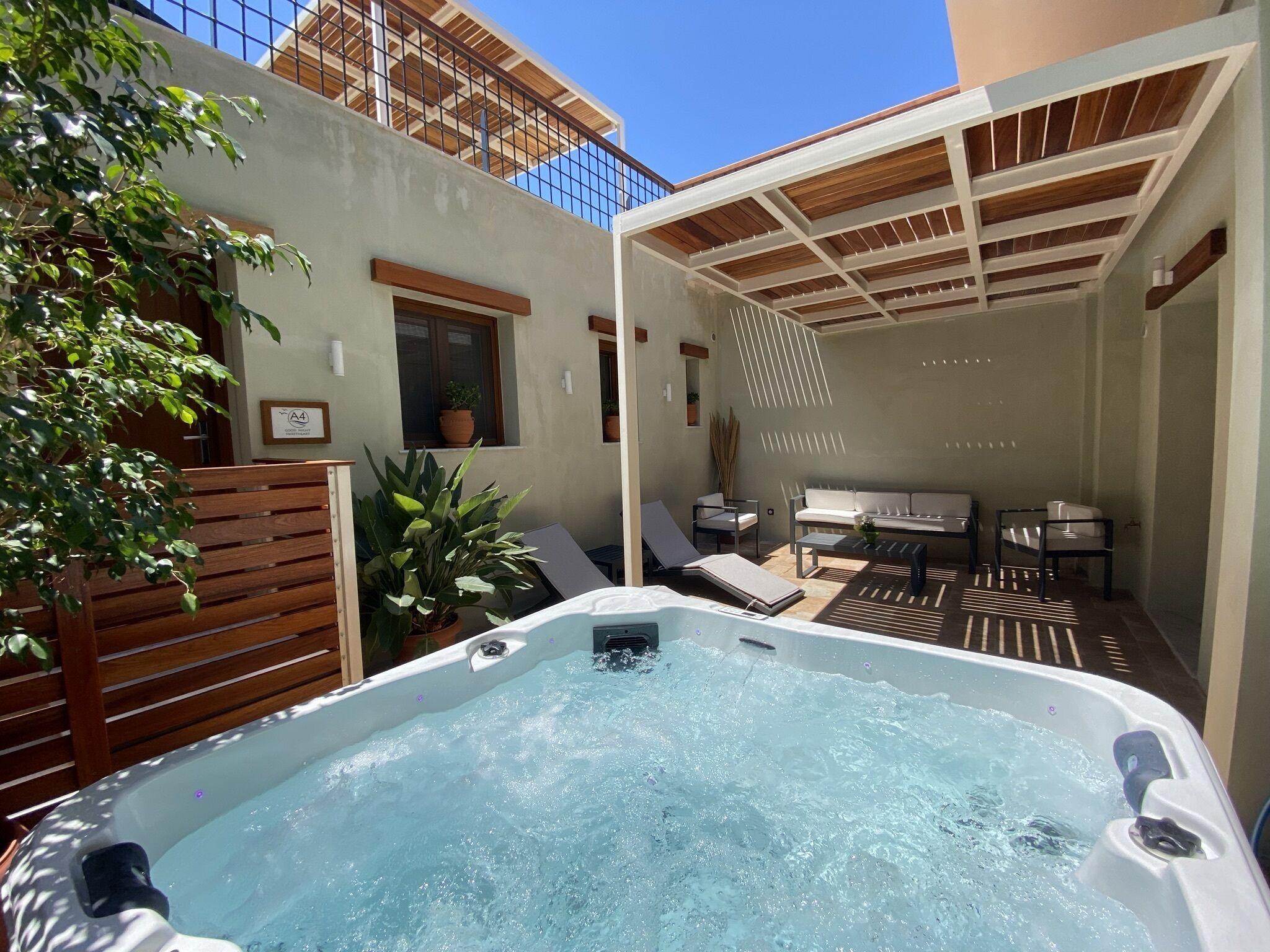 A hot tub in a sunlit outdoor area with lounge chairs and a pergola.