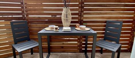 An outdoor patio area with a table and two chairs, a vase with branches, and a wooden slatted wall.