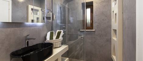 Un baño moderno con ducha de vidrio, tocador blanco y lavamanos negro, y un espejo.