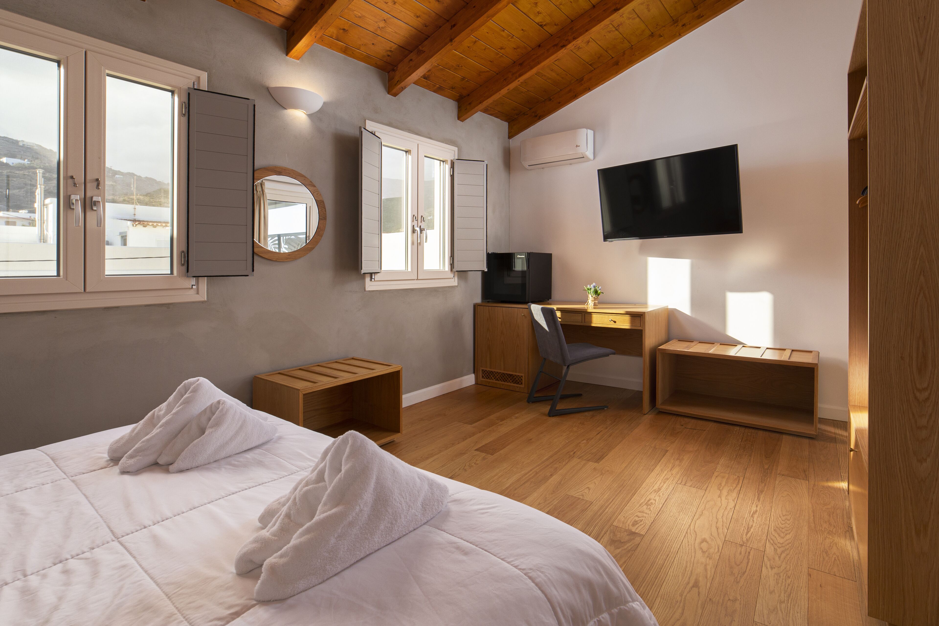 Un dormitorio con una cama, un escritorio, una silla, un televisor y una ventana con contraventanas.