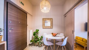 Una camera d'albergo moderna con una porta in legno, un tavolino rotondo con sedie, una pianta in vaso, una ciotola di frutta e un divano giallo.