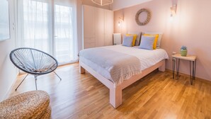 Una camera da letto con un letto, una sedia, un comodino, una lampada a parete e una finestra con tende.