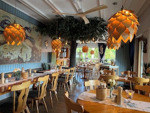 L’intérieur d’un restaurant est aménagé avec des meubles en bois, des lampes suspendues et une fresque murale.