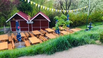 A rustic outdoor seating area with wooden benches and tables, a small building labeled 'Biergarten', and a fountain.