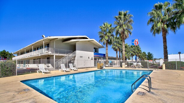 A pool area with lounge chairs, a building with a balcony, and palm trees.