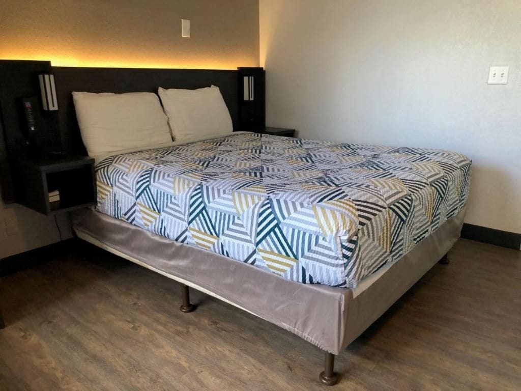 A bed with a patterned bedspread, a nightstand, and a bedside table with a lamp.
