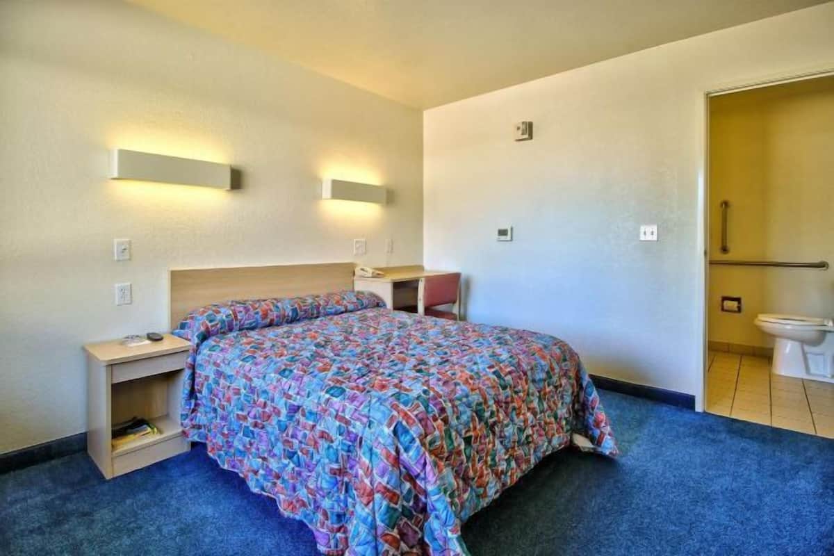A hotel room with a bed, bedside table, and a bathroom with a toilet and sink.
