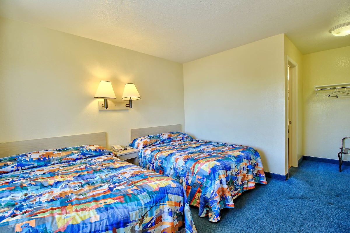 A hotel room with two beds, each with a colorful bedspread, a nightstand with a lamp, and a door leading to another room.