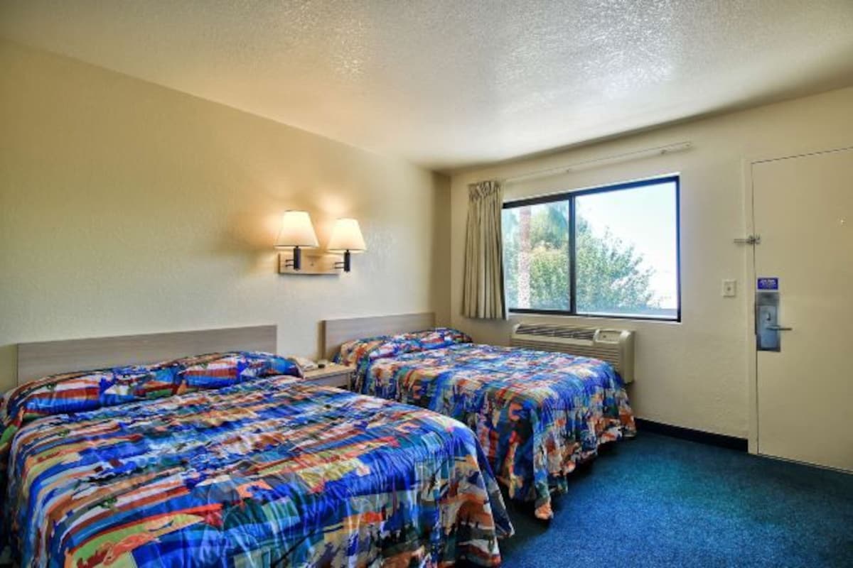 A hotel room with two beds, a window with curtains, a wall-mounted lamp, and a door.