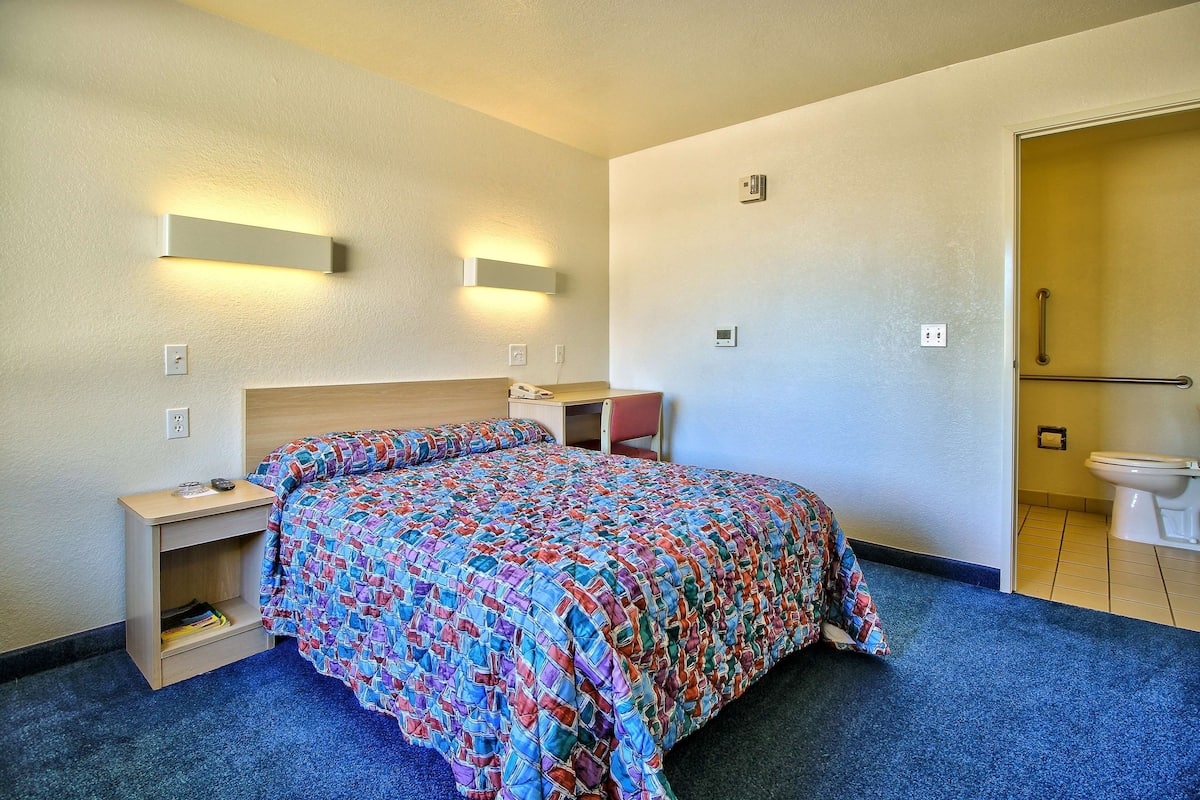 A hotel room with a bed, bedside table, lamp, and a bathroom with a toilet and sink.